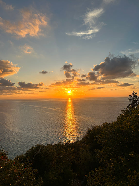 Golden sunset at Milos Beach on Lefkada Island, Greece, with the sun dipping below the horizon, casting warm hues over the serene turquoise waters and soft sandy shoreline, creating a picturesque and tranquil scene.